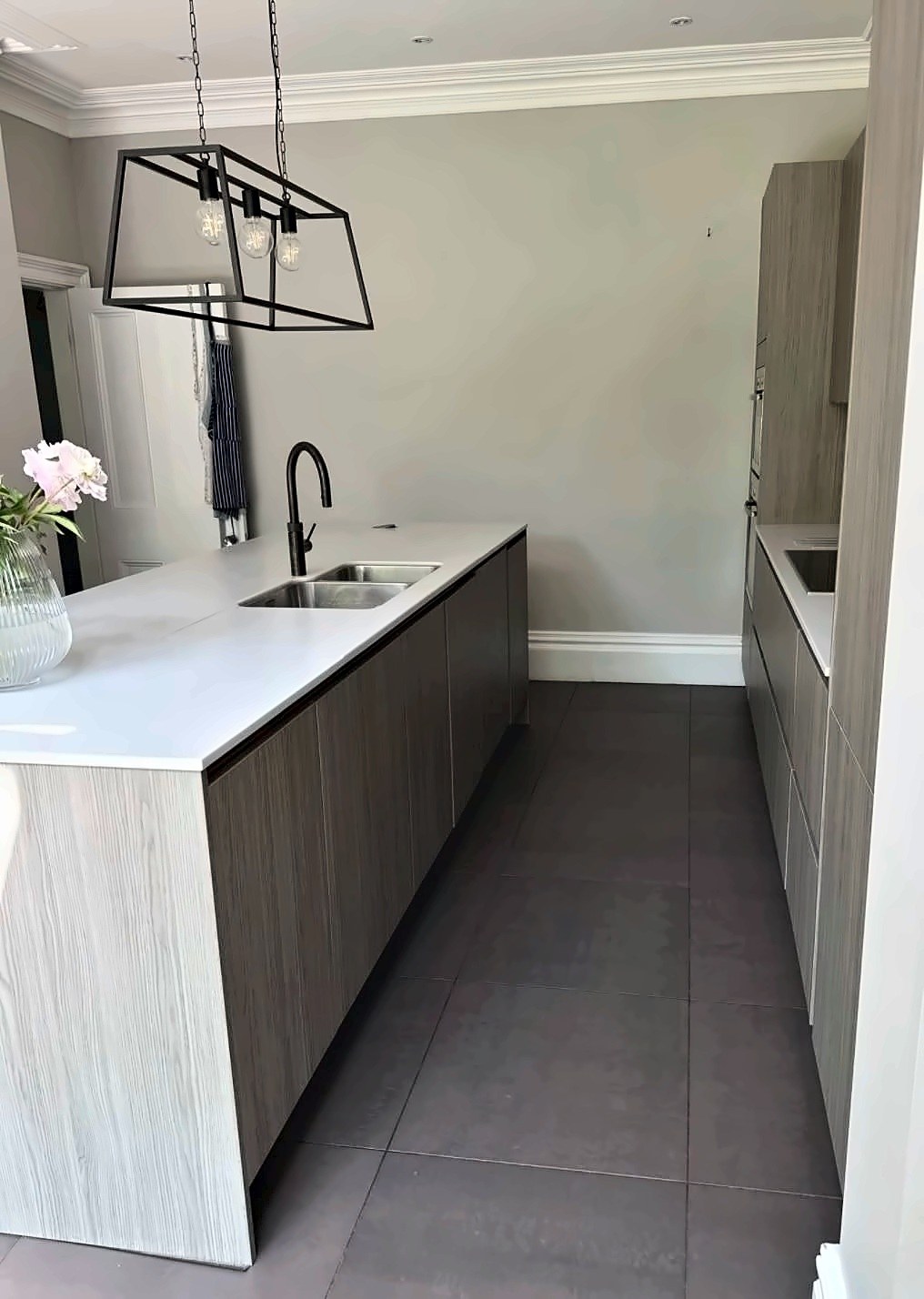 Grey woodgrain kitchen with a long white quartz island, undermount double sink and black lantern pendants.