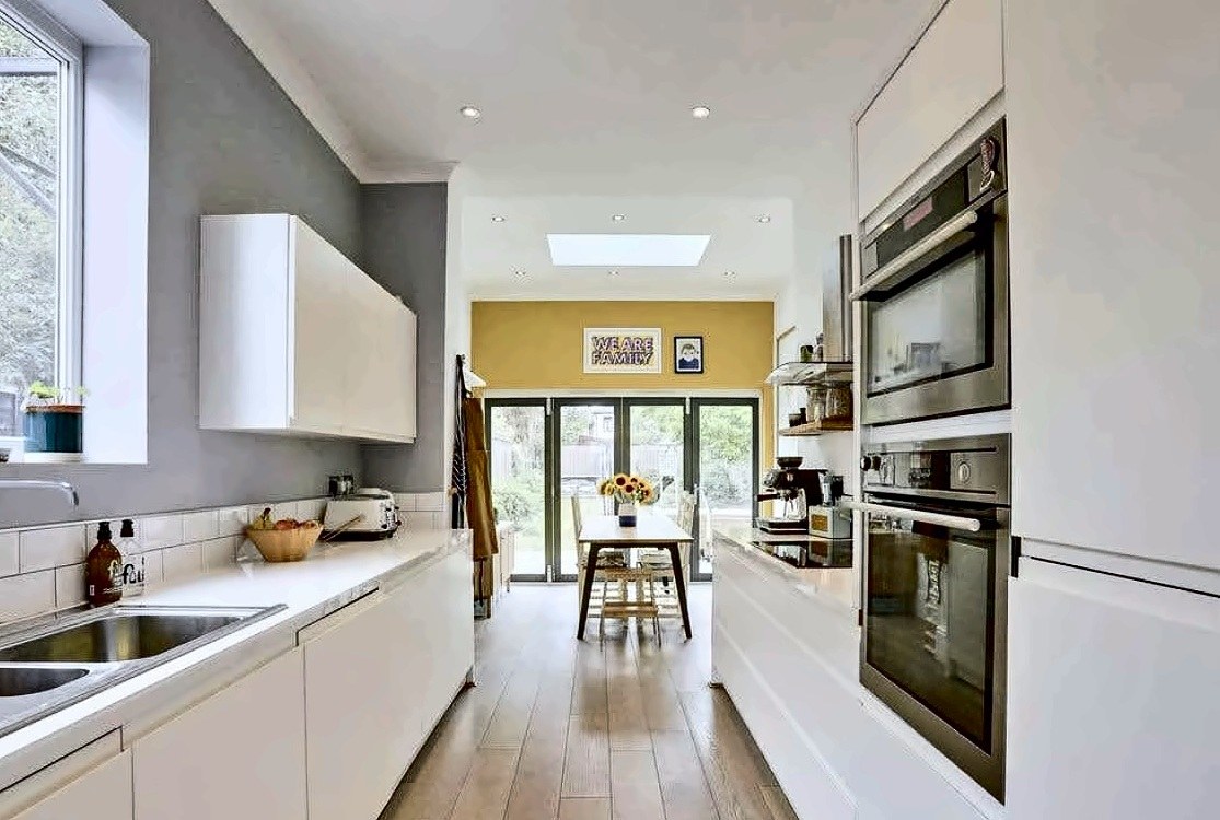 White handleless galley kitchen with oak flooring, double ovens and bifold doors to the garden.