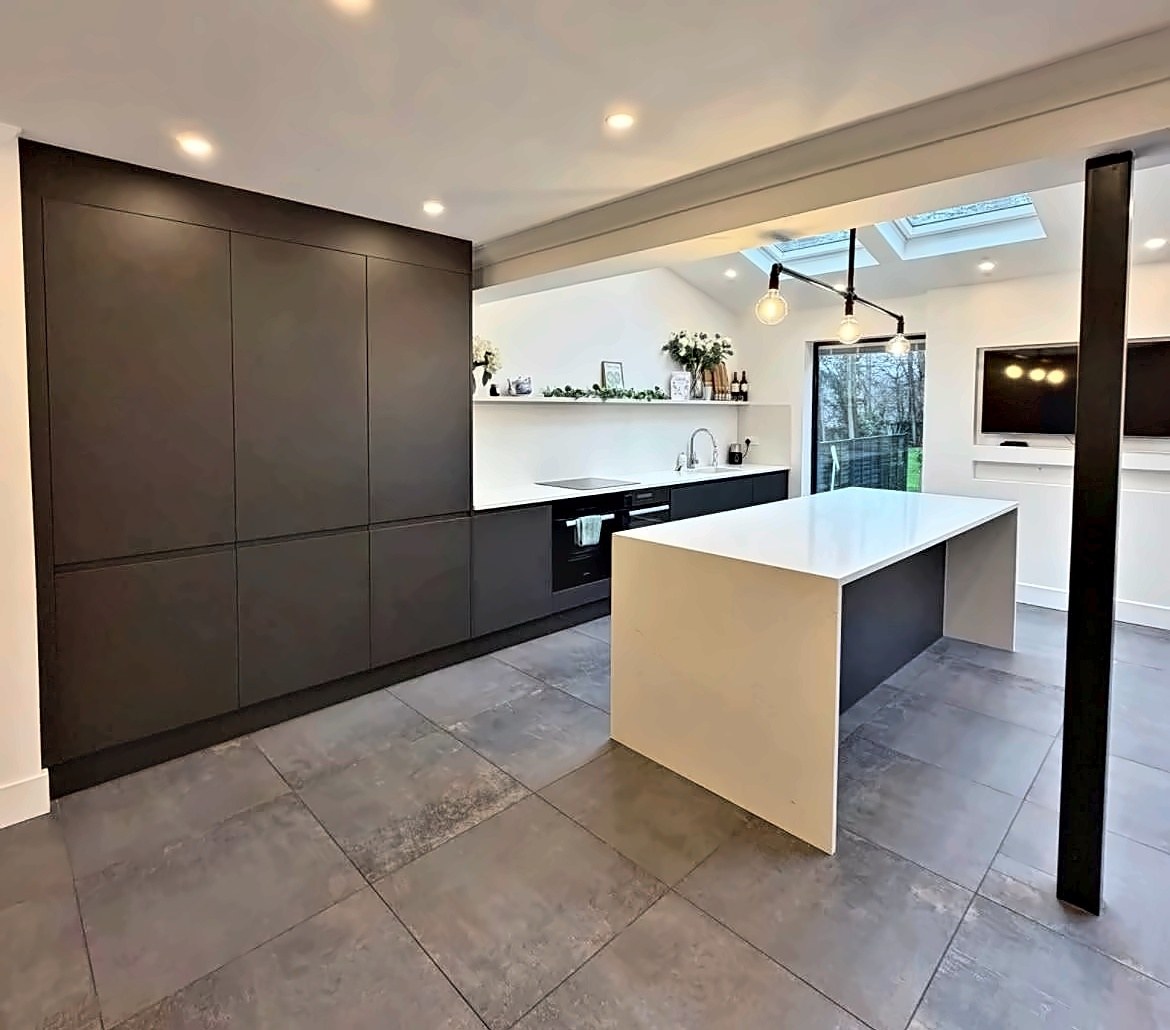 Graphite handleless kitchen with a waterfall quartz island, marble splashback and roof lanterns.