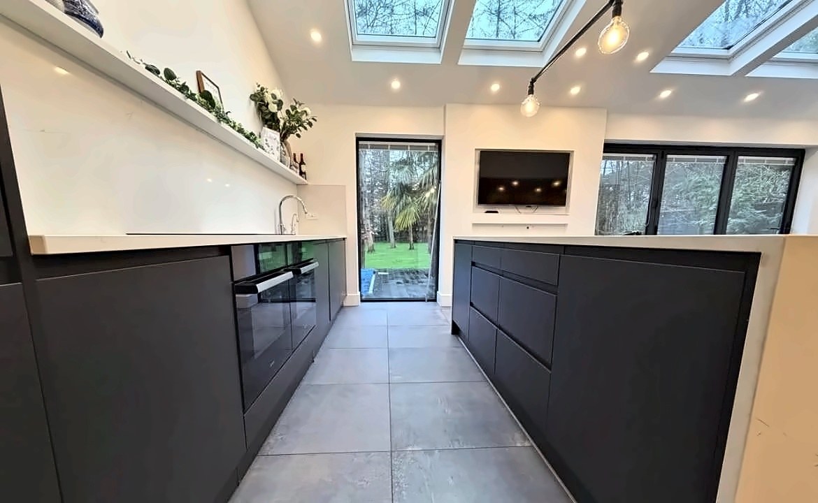 Graphite handleless galley kitchen looking through to the garden, with roof lanterns and a stone worktop.